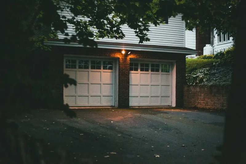 A garage door on a clapboard house, lit after dark.